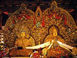 Tibet Lhasa 04 05 Potala Dalai Lama 5 and Shakyamuni In the Chapel of the Holy Born are two similarly sized statues sharing a joint throne, Shakyamuni in solid gold and the Great Fifth Dalai Lama in silver. The toranas behind the statues are finely carved with garuda and female subterranean figures. Shakyamuni was based on the Jowo Shakyamuni in the Jokhang Temple. The Fifth wears the Gelugpa yellow hat with his right hand in the teaching mudra and his left hand holding the dharma wheel.